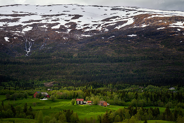 A tranquil Norwegian homes lie beneath majestic, snow-touched mountains.