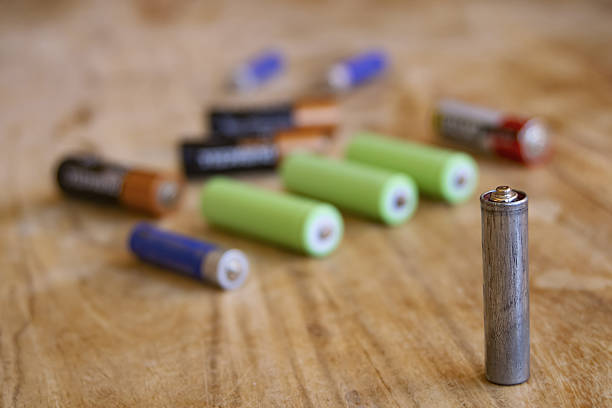 old depleted aa batteries in various colors on wood surface, focused on single battery in foreground, illustrating electronic waste and recycling needs
