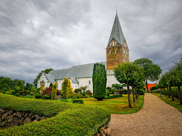 Mogeltonder Church stands majestically amid lush gardens and stone paths on a cloudy day in Denmark.