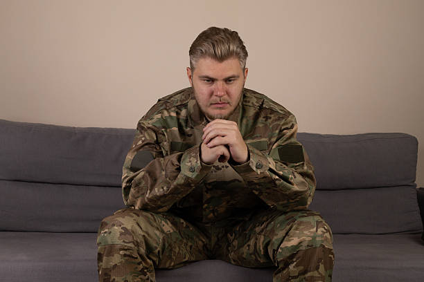 istock Man in camouflage sitting on a couch, holding a map and looking at a compass 2242956498