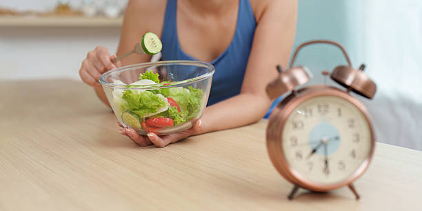 istock Food Wellness: Woman preparing fresh salad with clock in view 2242960357