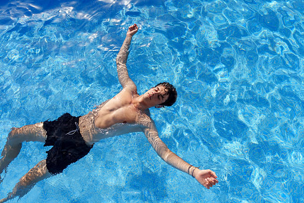 Young man floating face up, eyes closed, relaxing in the refreshing blue water of a swimming pool on a summer day