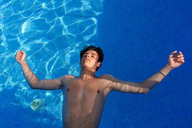 Young man wearing swimwear floating on his back in a bright blue swimming pool, relaxing with eyes closed