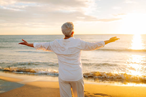 istock An older woman with gray hair walks along a sunlit sandy beach. 2242963607