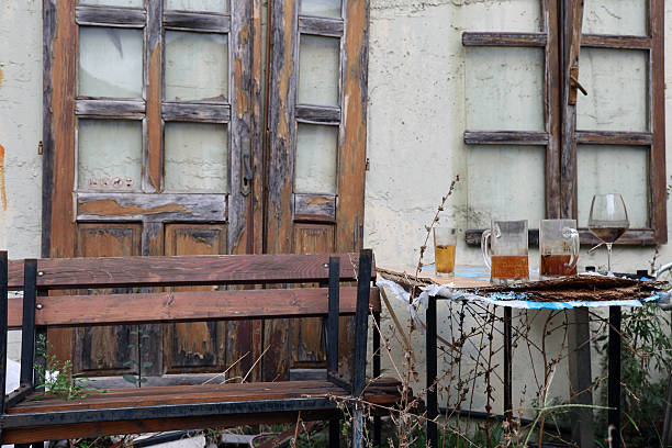 Rustic outdoor scene with weathered wooden bench, old doors, and drinks on a table, evoking nostalgia and a sense of forgotten charm, perfect for vintage themes