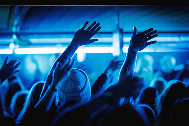 Group of people with hands raised during a live concert under vibrant blue stage lighting.
