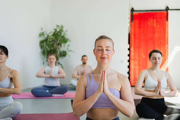 istock Yoga mindfulness meditation. Group of sporty people doing exercise in studio for class for yoga wellness mindfulness meditation. Men women practicing yoga sitting in lotus pose meditating relaxing. 2242976103