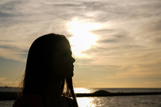 Depicting serenity and creative imagination, this silhouette captures a woman grasping sunlight during a stunning seaside sunset.