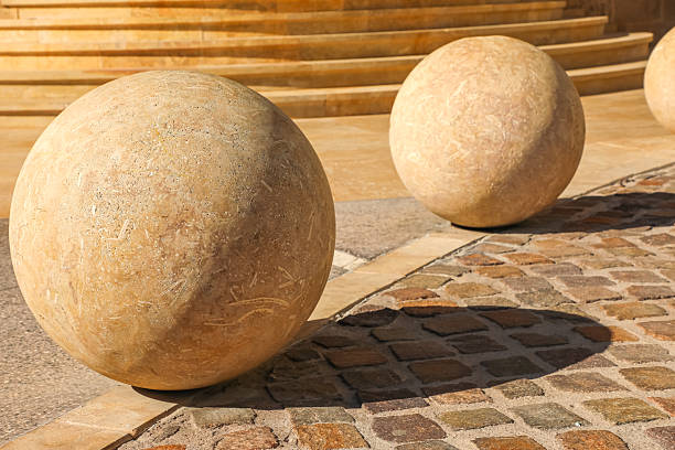 Large decorative stone spheres on a paved street with warm sunlight and architectural steps in the background. Urban design and modern landscaping elements.