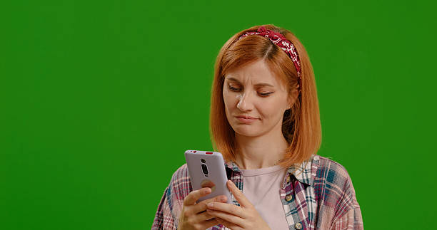 istock Pretty lady working on smartphone or scrolling looking suspiciously on green screen background. 2242982143