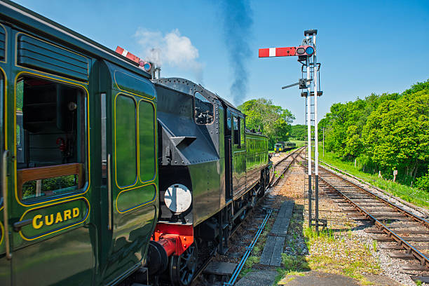 Old historical traditional heritage steam engine locomotve train travelling on tracks in rural countryside setting with signal