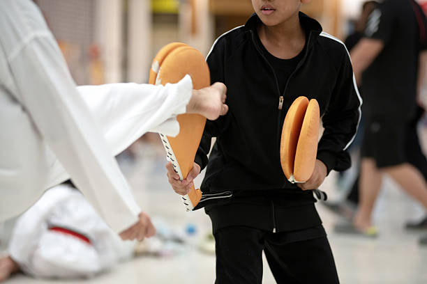 Asian boy and girl athletes practicing Taekwondo while waiting for the competition. A boy holds a Taekwondo target for a girl to kick. Training or exercise with Taekwondo sport, selective focus