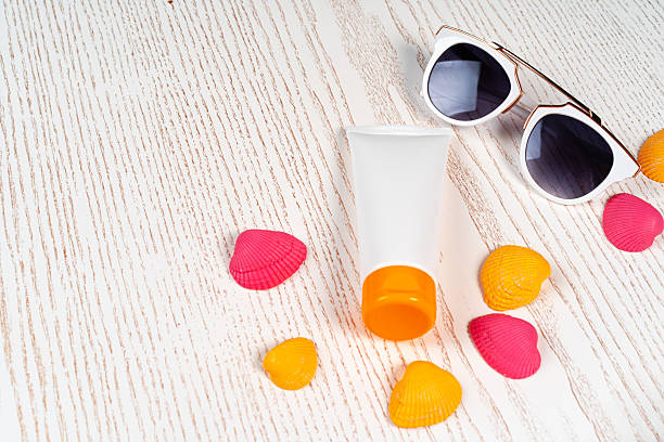 Sunblock lotion with colored seashells on wooden board, copy space