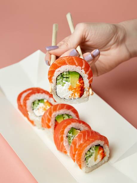istock Hand holding sushi roll with chopsticks. 2243002576