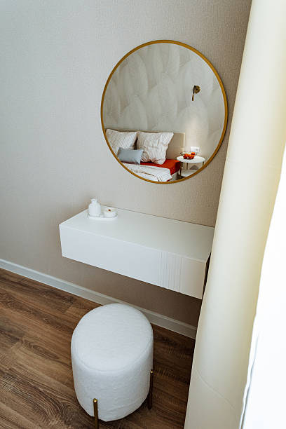 istock A beautifully designed bedroom featuring a stylish round mirror alongside a cozy white ottoman, creating a perfect mix of elegance and comfort in the overall interior space 2243010998