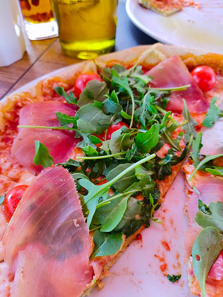 Enjoy a slice of delicious Italian pizza topped with fresh arugula, prosciutto, and cherry tomatoes. Perfect for a restaurant menu or food blog!