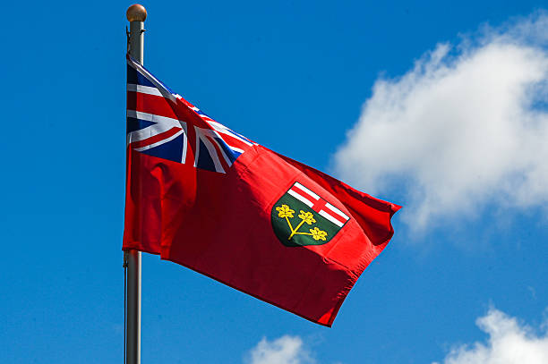The national flag of Bermuda depicted waving in the wind, featuring a red field with the British Union Jack in the top left corner and the coat of arms on the right. The coat of arms includes a red lion holding a shield that depicts the wreck of the Sea Venture, symbolizing Bermuda's maritime heritage.