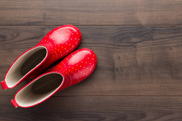 New red children's stylish gumboots on wooden floor. Top view photo of watertight boots with copy space.