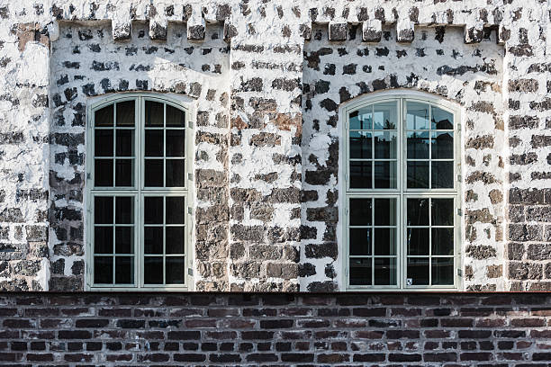 Two large arched windows set in an old industrial building in Sweden reveal the textured stone wall and the history of the structure. The setting reflects early 20th-century design.