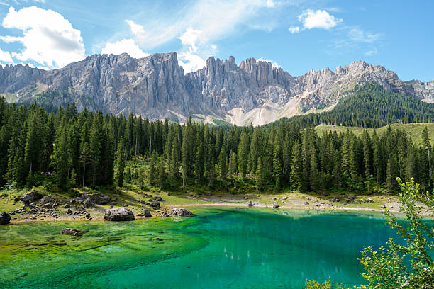 Scenic view of the famous Lago di Carezza (Karersee) in the Dolomites, northern Italy. The emerald lake is surrounded by dense pine forest and overlooked by the impressive Latemar mountain range. A peaceful alpine landscape capturing the beauty of nature, reflection, and the harmony between water, forest, and rock — perfect for concepts of wilderness, travel, and eco-tourism.