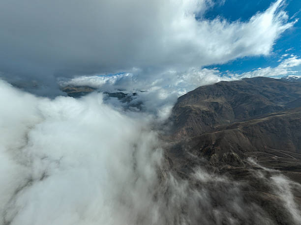 Close aerial shot of a rugged mountain range with dark, heavy clouds and thick white fog rolling dramatically over the peaks and slopes
