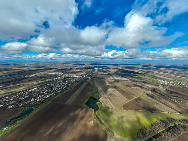 High angle aerial view of patterned fields and a village, with intense shadows from large clouds dramatically splitting the landscape into light and dark sections