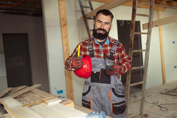 A man with an electric drill in his hands. The worker points with his finger. Hard hat and work vest.