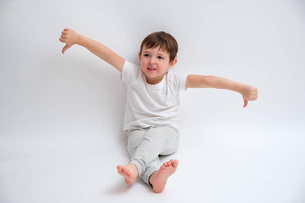 istock Little boy showing thumbs down gesture with both hands while sitting on white backdrop. Dislike or rejection concept for childhood experiences. Child aged 4 years (four years old) 2243041074