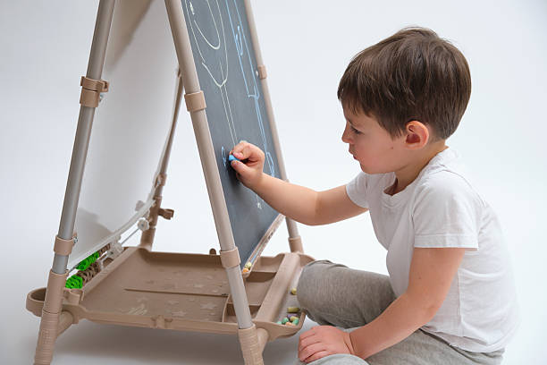istock Cute boy drawing on a chalkboard with blue chalk. Child engaged in creative learning and artistic development. Early childhood education activity. Child aged 4 years (four years old) 2243041080