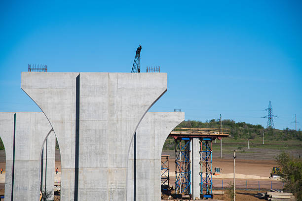 Construction of the interchange of a road bridge across the river. Builders and construction equipment on the construction site. The support of the bridge against the blue sky.