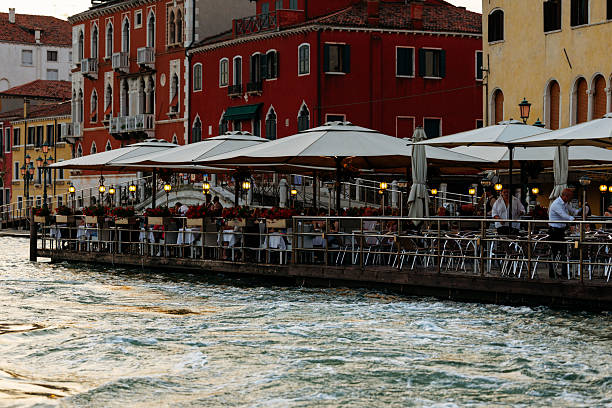 Venice, Italy - June 23, 2025: Waterfront restaurant in Venice offers outdoor dining with umbrellas, surrounded by colorful buildings and a serene canal atmosphere