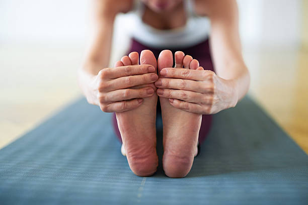 A person performs a seated forward bend, gripping both feet in a calm yoga practice. The close-up emphasizes flexibility, balance, and mindful exercise on a blue gym mat.
