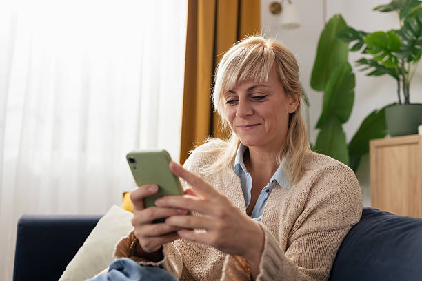 istock Mature woman smiling using smartphone on couch 2243090610