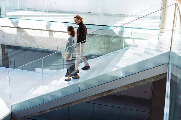 Two Professionals Walk Down Glass Staircase in Bright Modern Atrium, Business Context and Open Space