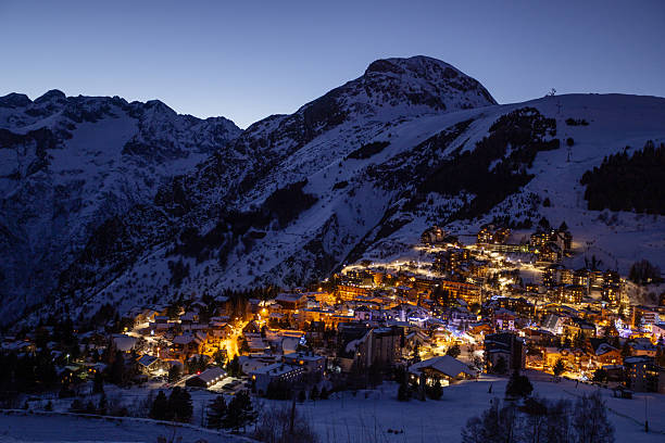 istock Night-time ski resort village glow warmly under alpine night sky 2243102445