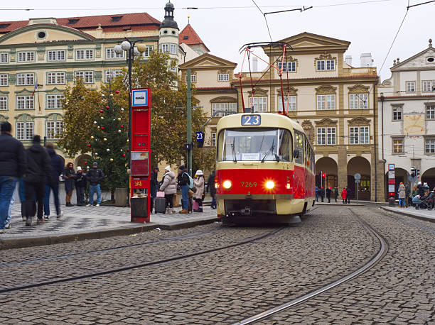 Prague, Czech Republic - December 13, 2024: Vintage red and cream tram traveling through cobblestone square with historic European architecture