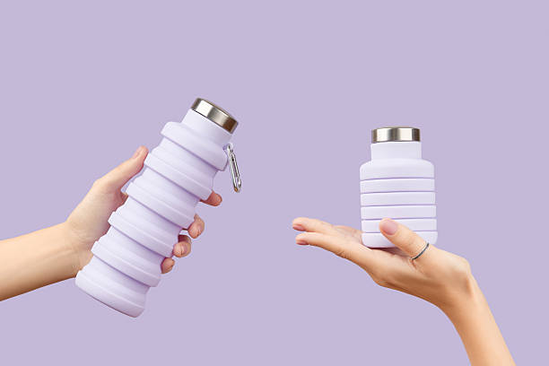 istock Womans hand holding collapsible reusable lilac water bottle on purple background. Zero waste 2243106808