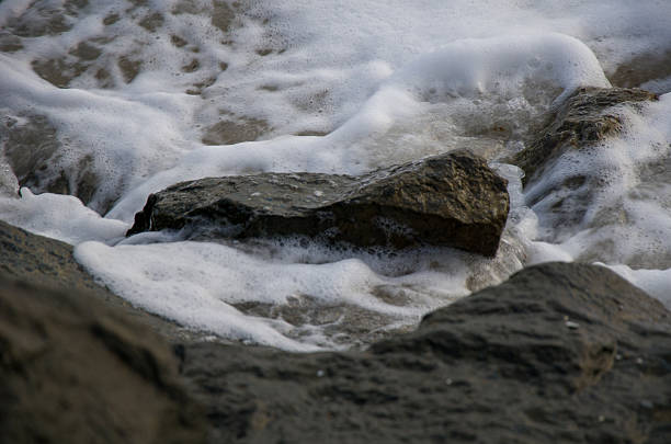 istock Sea Foam Swirling Around Dark Coastal Rocks 2243109490