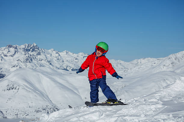 istock Kid in red jacket skis atop a snow-covered ridge under blue sky 2243112084