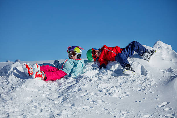 istock Two children lie cheerfully atop a snowdrift in winter jackets 2243112097