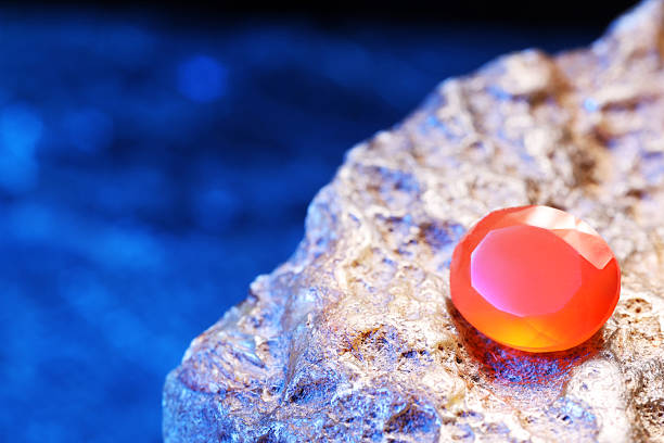 Beautiful shiny orange gemstone on stone against blue background, space for text