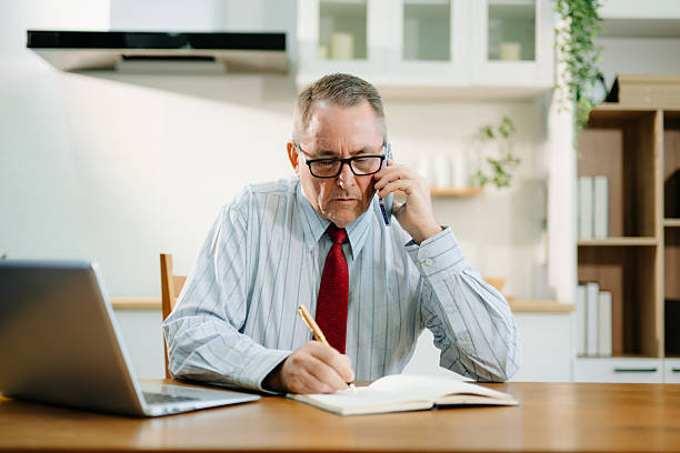 istock Mature Businessman using laptop while sitting at home. man sitting in kitchen 2243119465