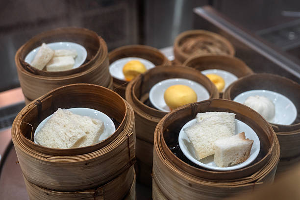 A close-up view of assorted soft bread and dim sum items served in traditional bamboo steamers at a buffet station. The setup includes buns and bread pieces placed in small bowls inside the steam baskets, creating a warm and authentic Asian dining atmosphere.