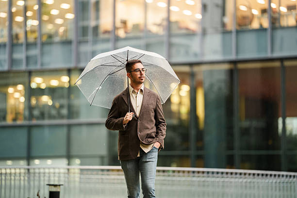 istock Man walking with umbrella near modern glass building 2243130398