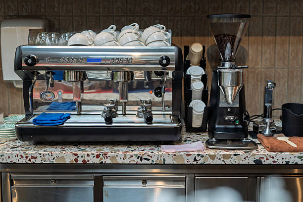Coffee maker with black handle pours hot coffee into two white ceramic cups. Close-up viewed from the side