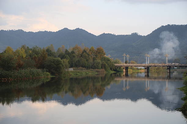istock a river with green trees on both sides, reflecting the distant mountains and clouds in an autumn evening. 2243134252