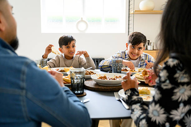 istock Two British Pakistani boys sitting at dining table with parents, smiling and having fun 2243163015
