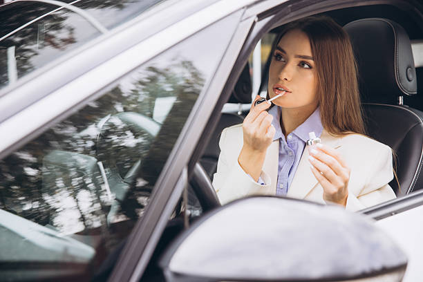 istock Elegant Woman Applying Lip Gloss in Car Interior 2243172764