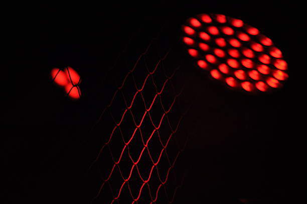 Red lights glow through a metal grate, creating an intriguing pattern against a dark background at night. The scene captures elements of urban life and industrial design.