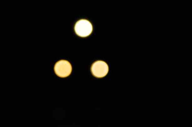 Three distinct lights glow in the darkness, with one large light above two smaller ones, creating an intriguing visual contrast in the night atmosphere.